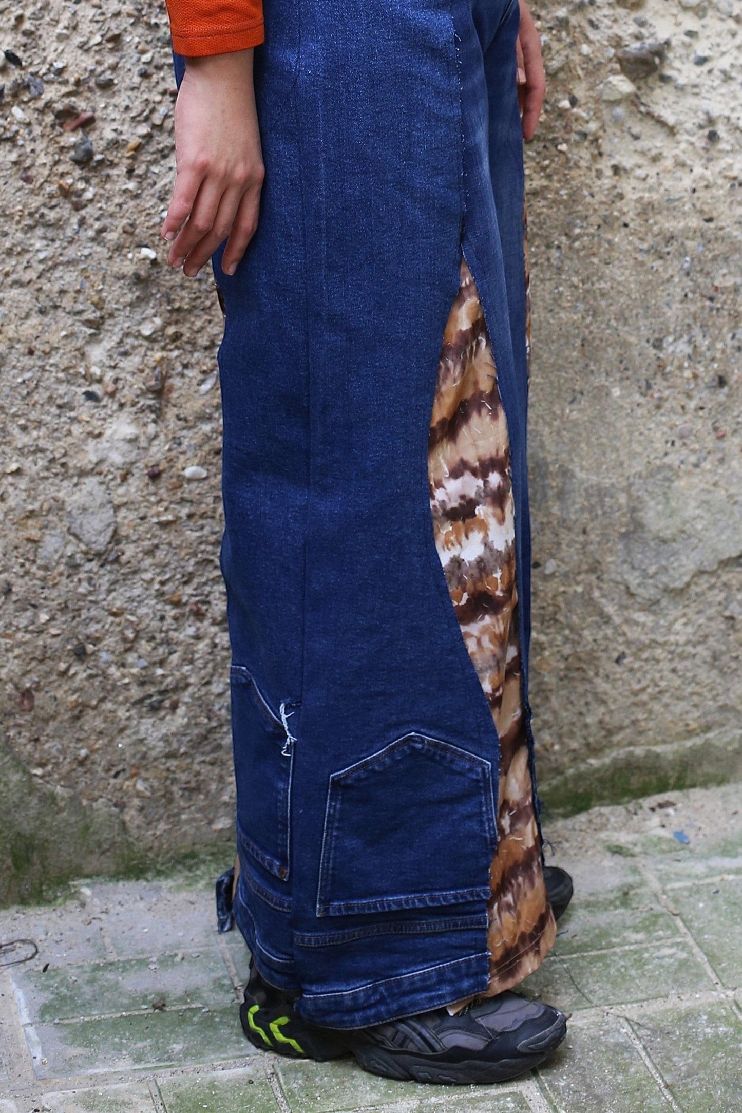 Thoughts Reworked blue denim wide leg pants with brown and white tie-dye fabric inserts. Model is wearing orange top.