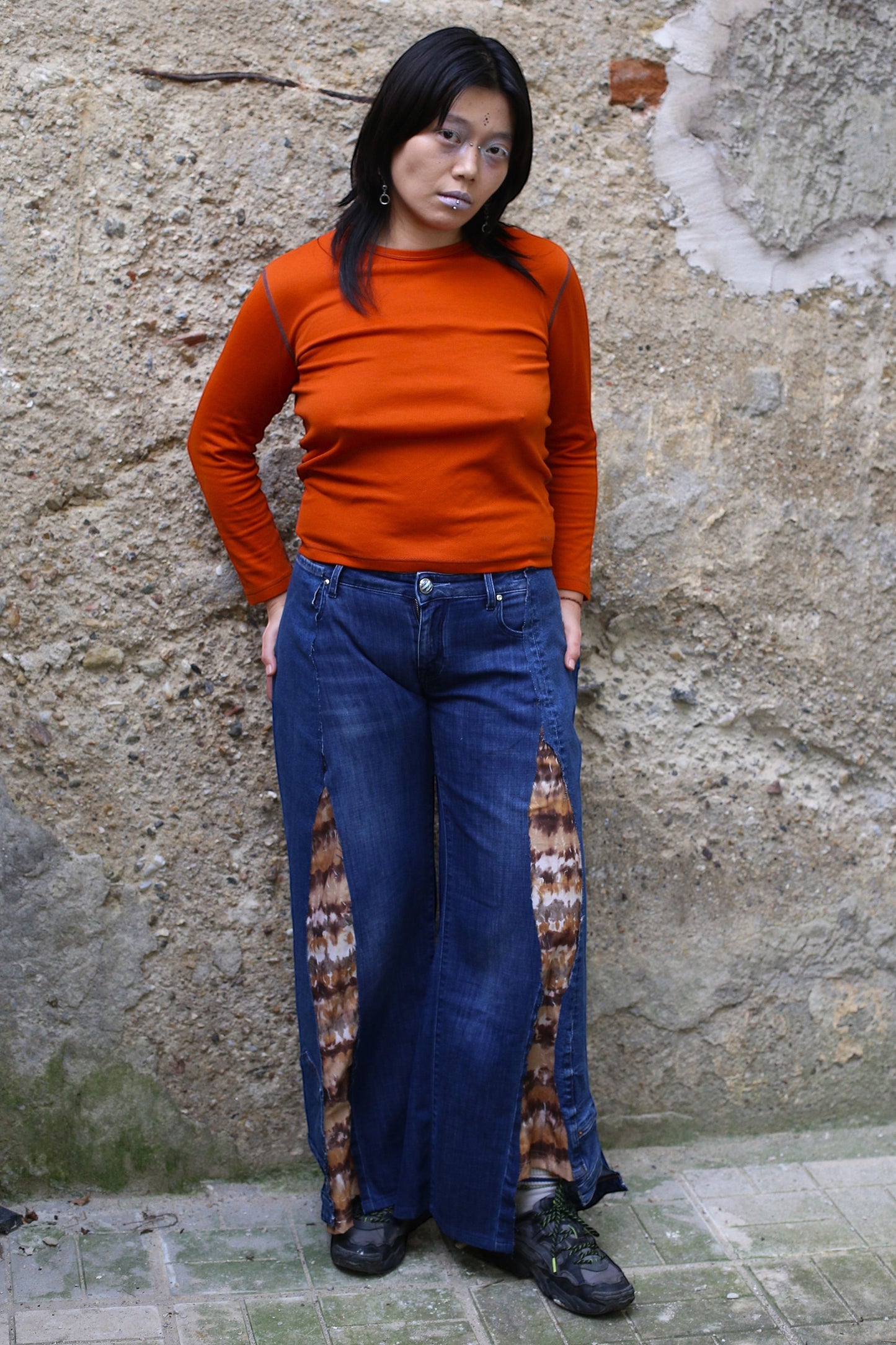 Thoughts Reworked blue denim wide leg pants with brown and white tie-dye fabric inserts on the side seams. Model is wearing an orange long-sleeve top.