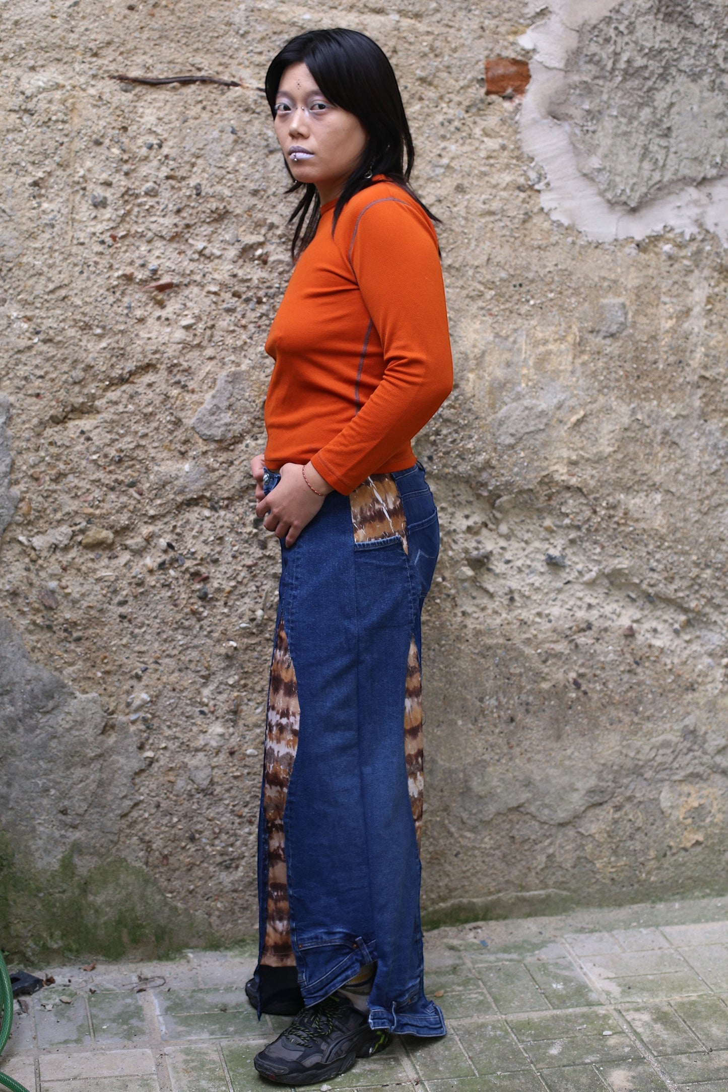 Thoughts Reworked wide leg jeans made from preloved denim and fabric panels with a feather-like print. Model is wearing an orange long-sleeve top.
